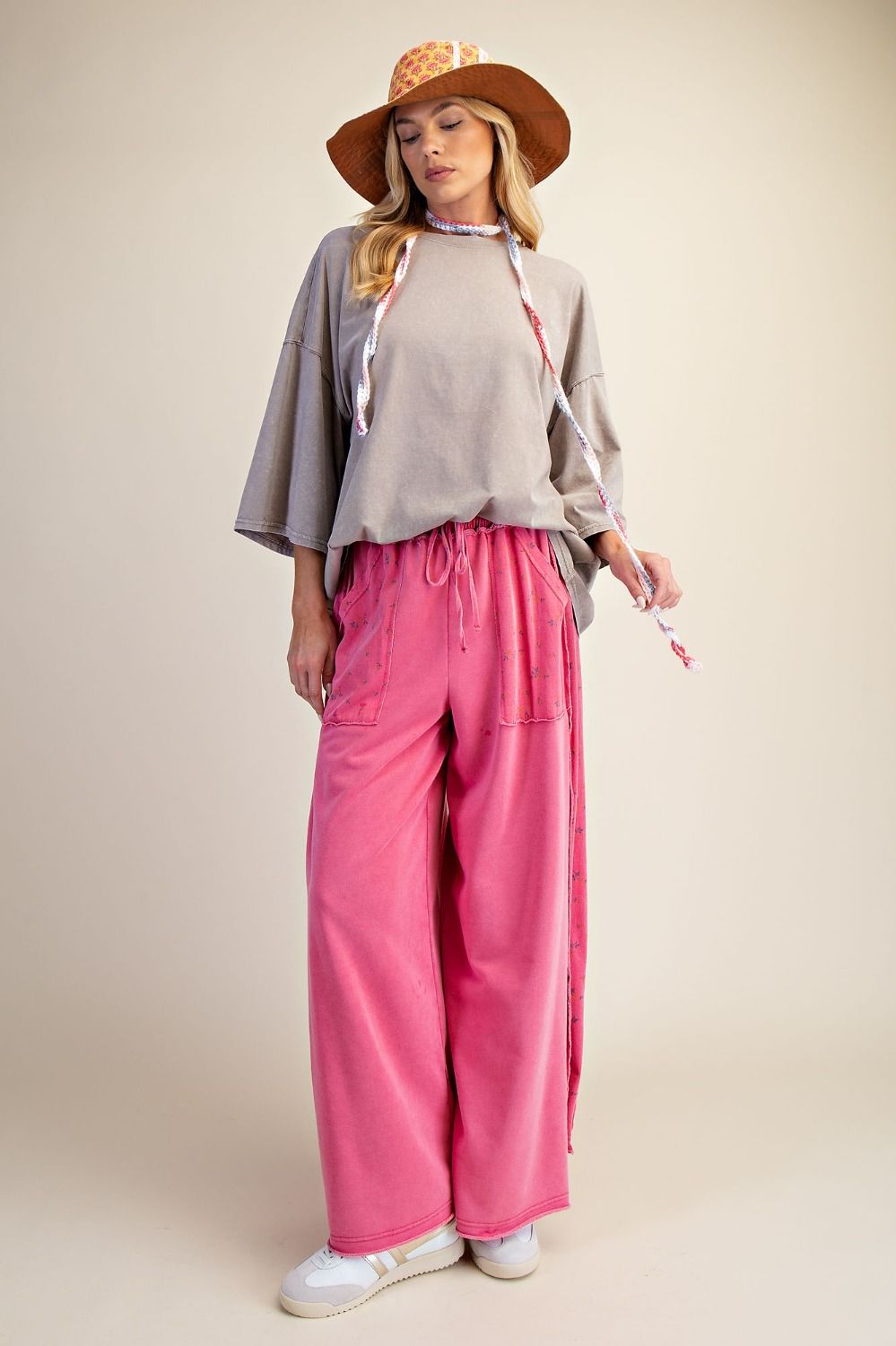Woman wearing a beige top, pink pants, and a straw hat on a beige background