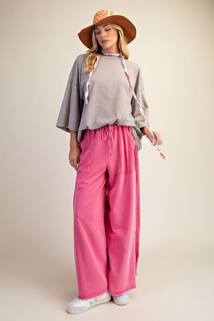 Woman wearing a beige top, pink pants, and a straw hat on a beige background