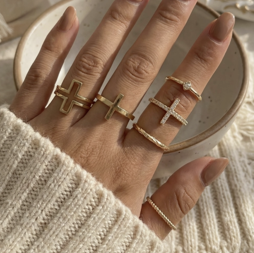 Womans hand wearing multiple gold rings with crosses 