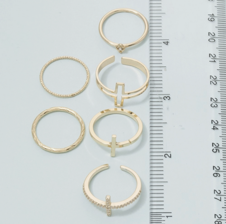 Six gold-toned rings of various styles and designs arranged next to a metal ruler for scale on a light blue background.