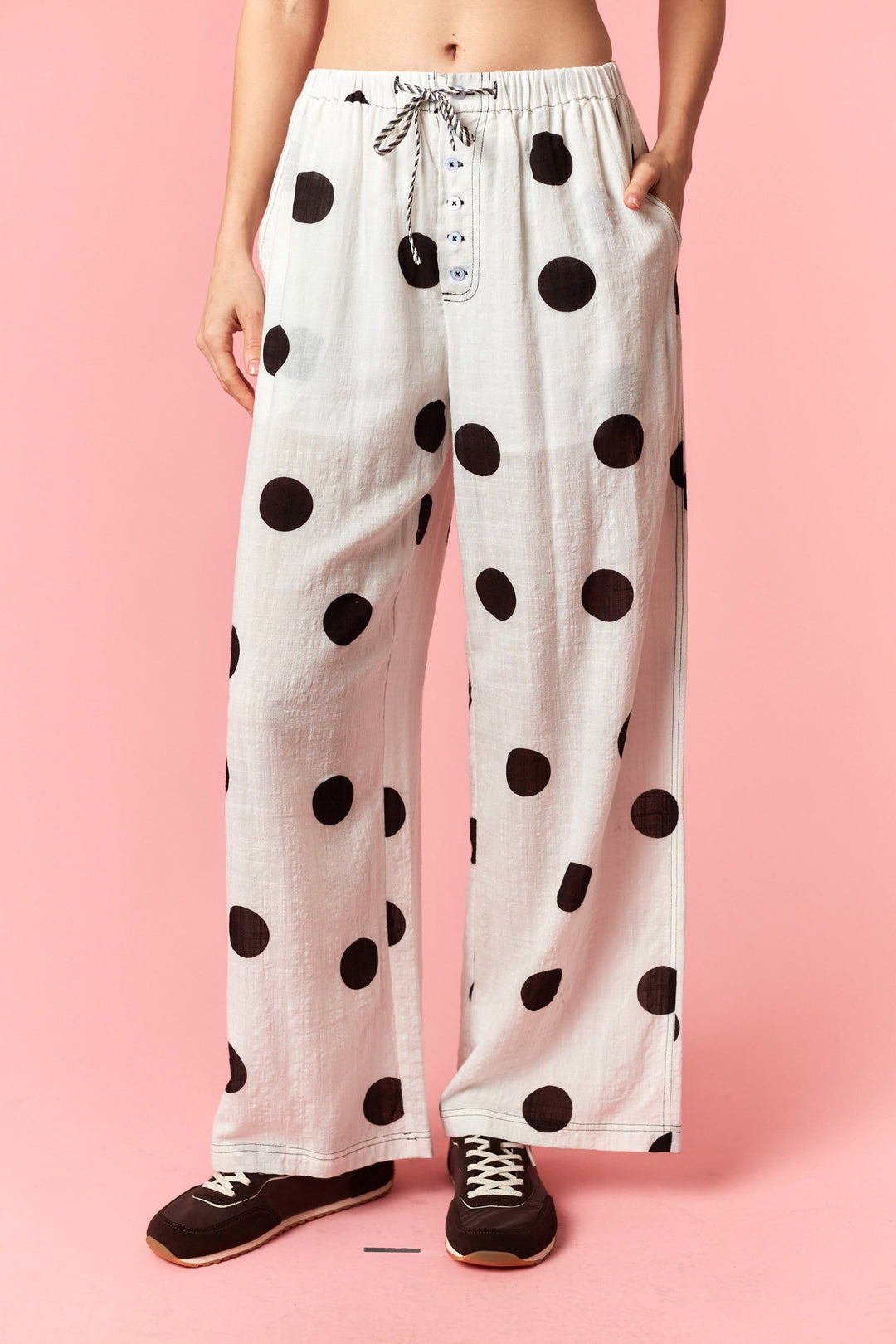 White pants with black polka dots worn by a person on a pink background