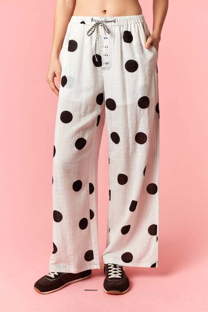 White pants with black polka dots worn by a person on a pink background