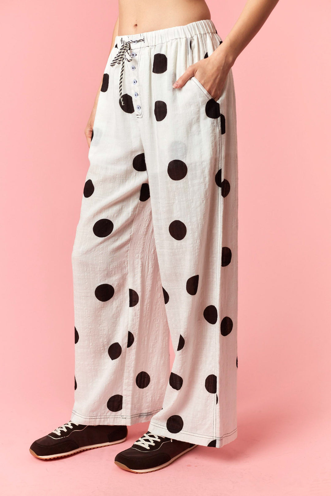 Person wearing white pants with black polka dots on a pink background