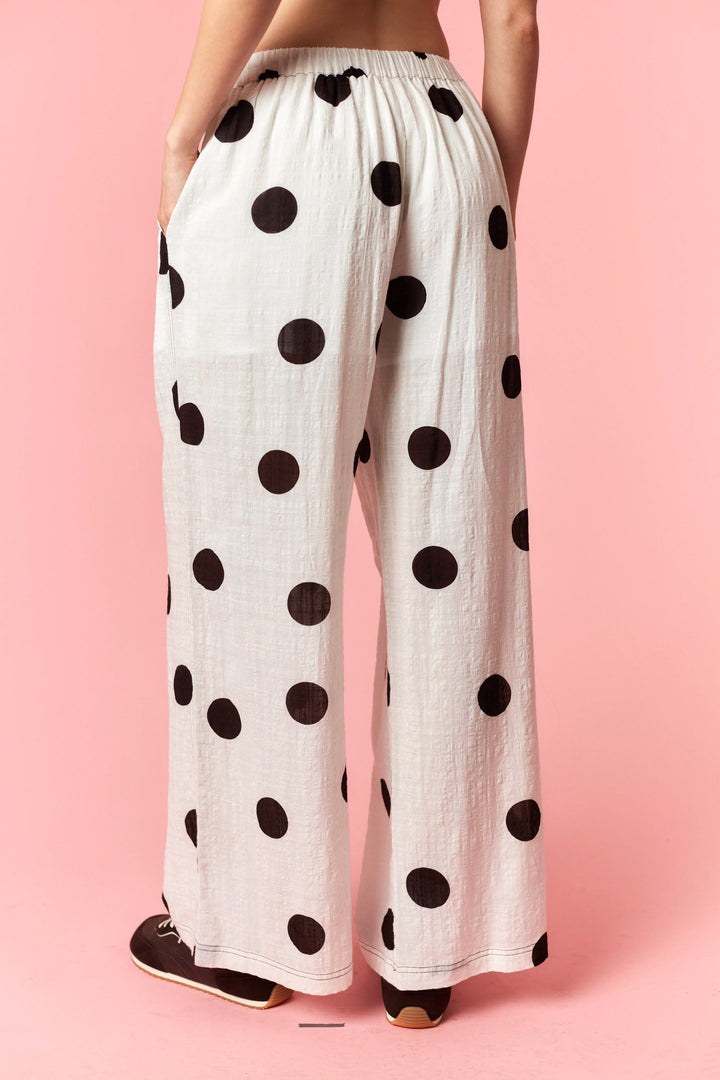 White pants with black polka dots worn by a person on a pink background