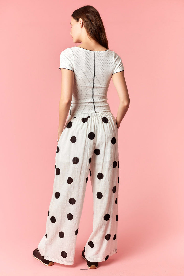 Woman wearing a white top and polka dot pants on a pink background