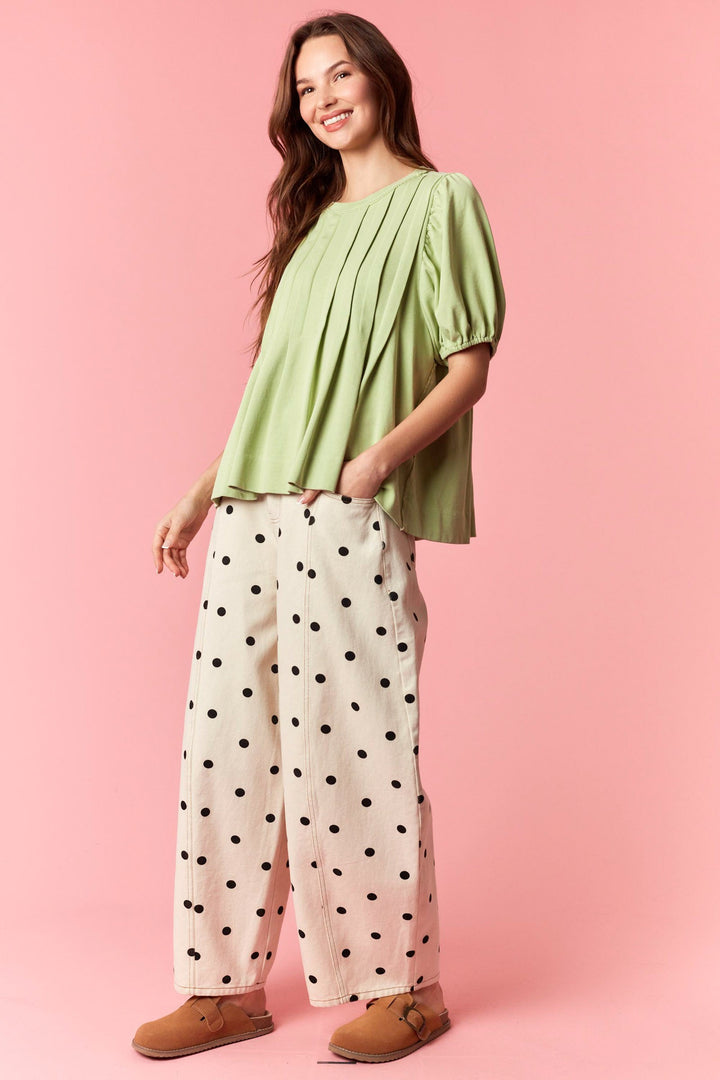 Woman wearing a green top and polka dot pants on a pink background