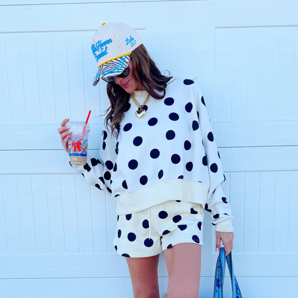 Person wearing a polka dot outfit with a colorful hat against a light blue wall.