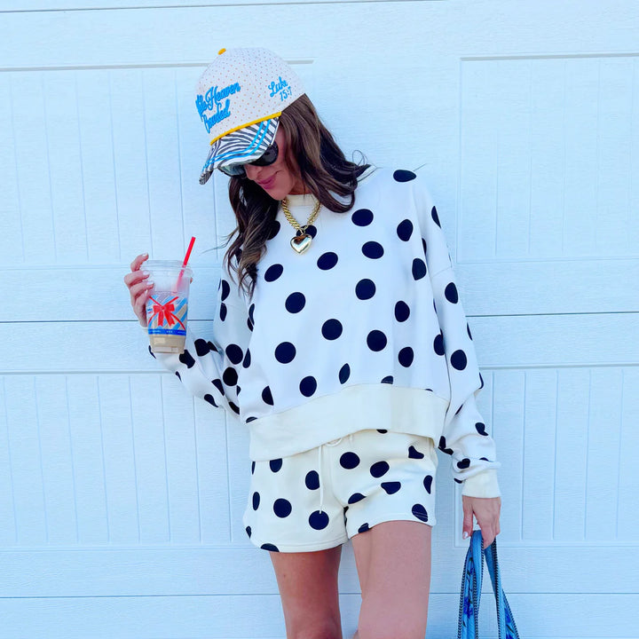 Person wearing a polka dot outfit with a colorful hat against a light blue wall.