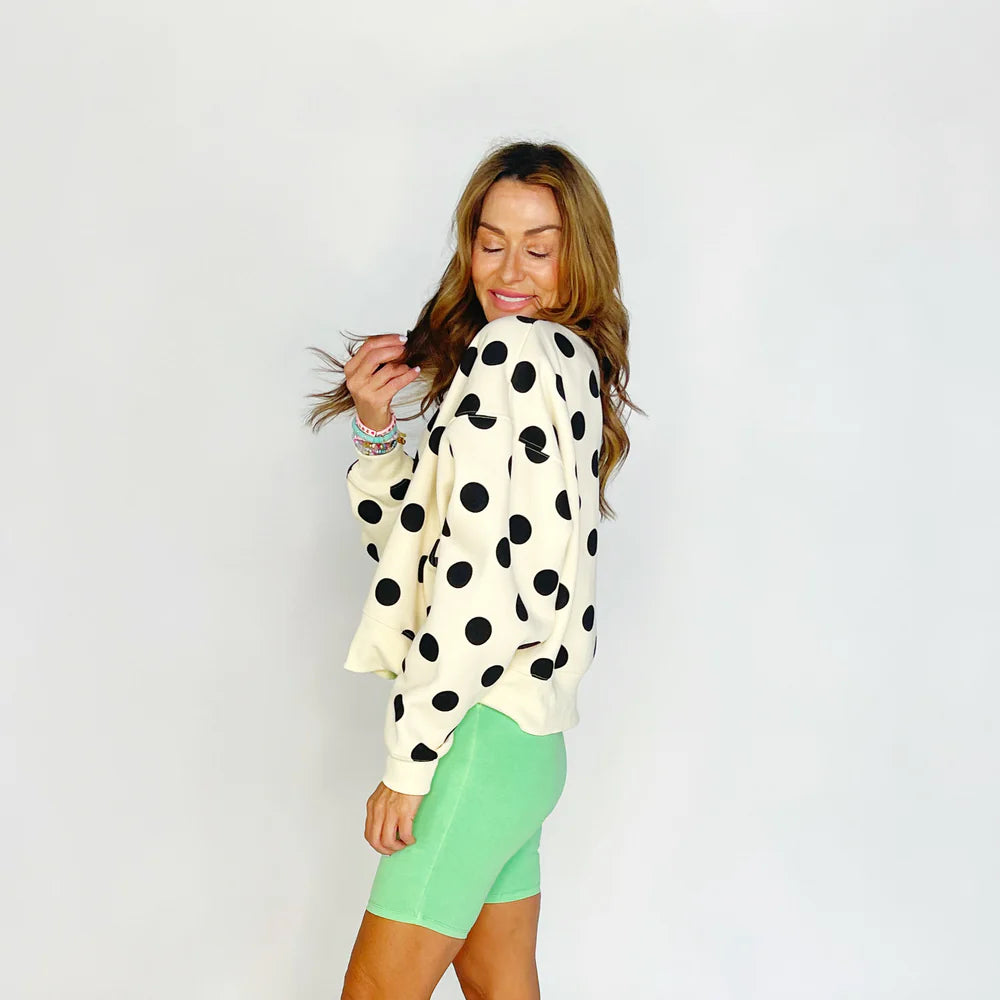 Woman wearing a polka dot sweater and green shorts on a plain background