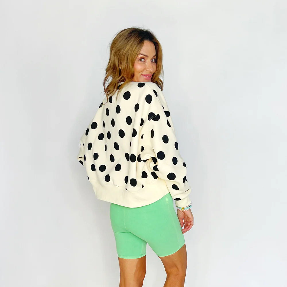 Woman wearing a polka dot jacket and green shorts on a plain background