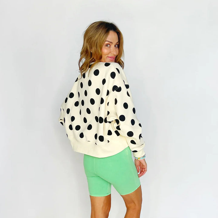 Woman wearing a polka dot jacket and green shorts on a plain background