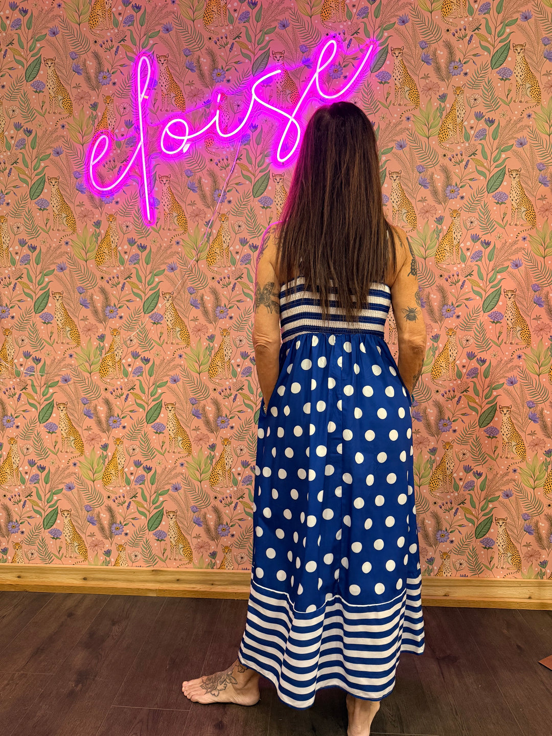 Back of woman wearing polka dot and stripe blue dress on pink floral background
