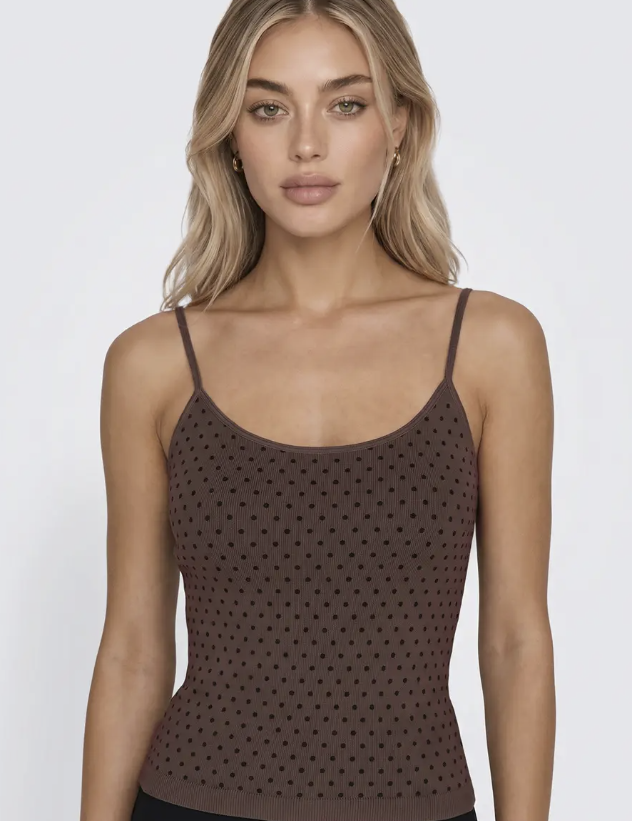 A woman wearing a brown knit camisole top with a perforated polka-dot pattern, shown against a plain light gray studio background.