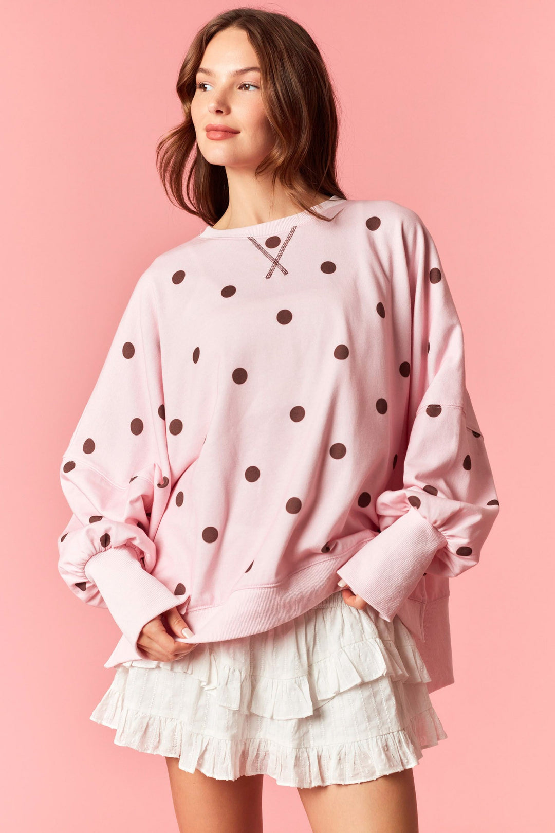 Woman wearing pink sweatshirt with burgundy polka dots on plain background