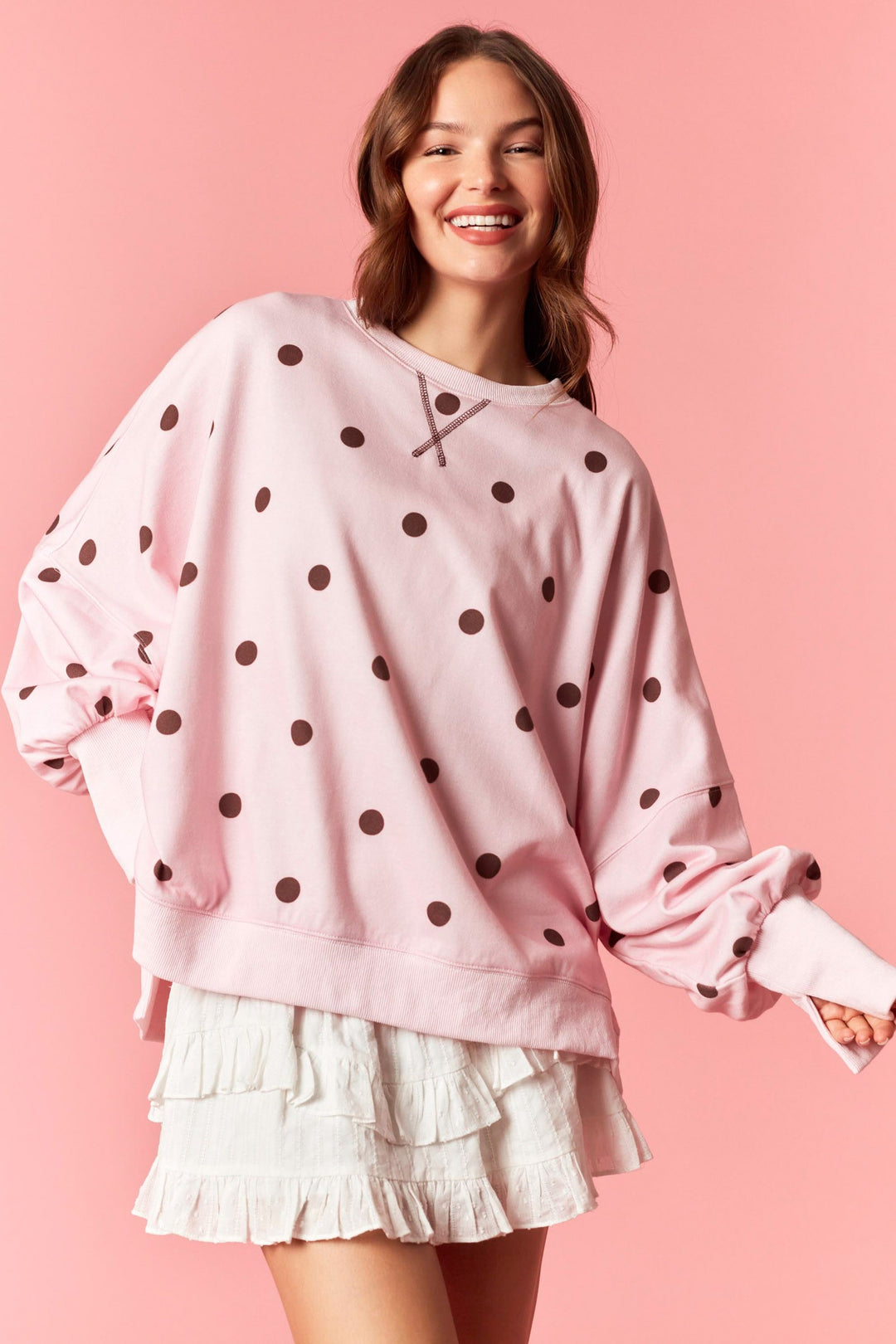 Woman wearing pink sweatshirt with burgundy polka dots and white mini skirt on plain background