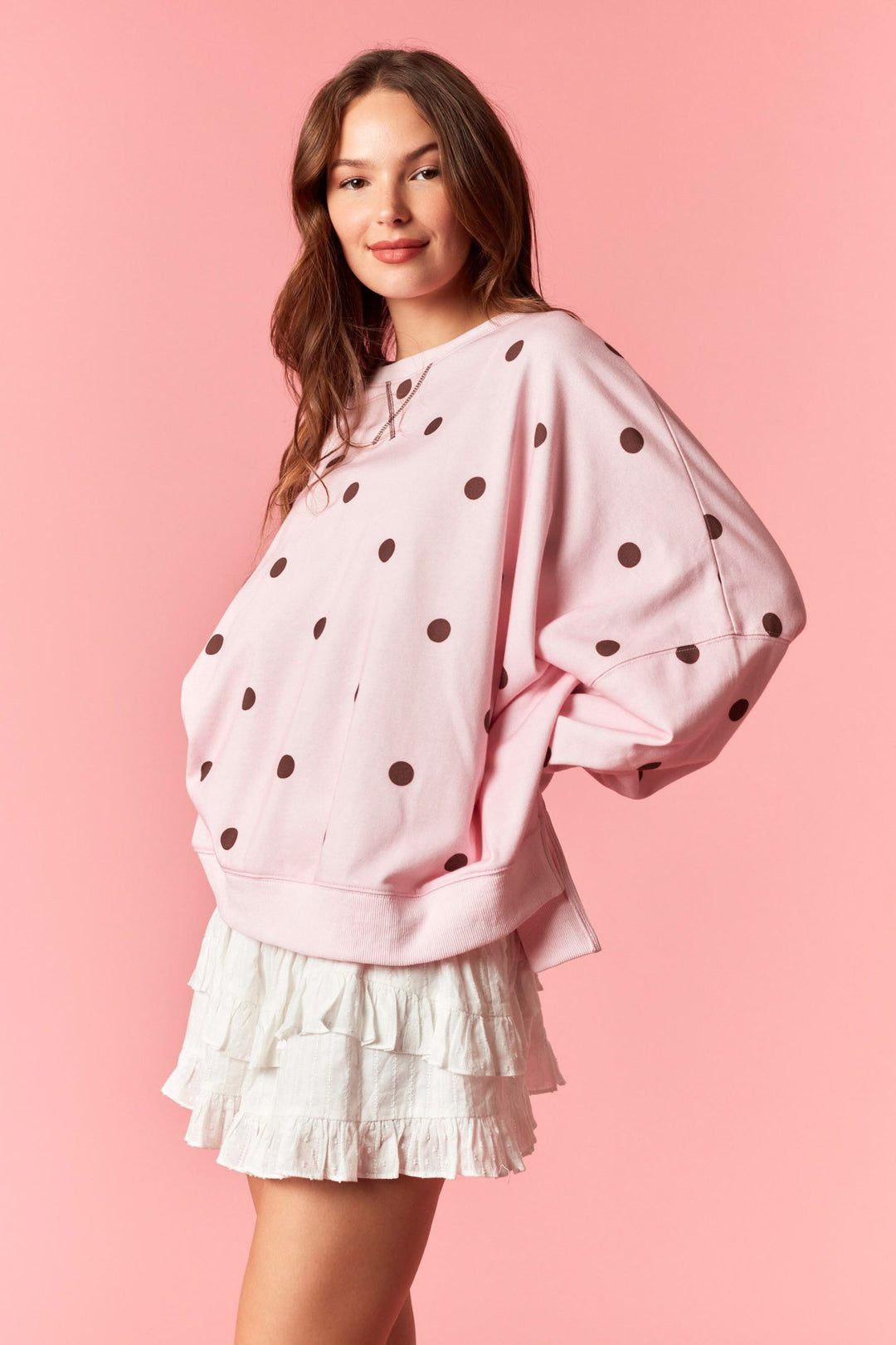 Woman wearing pink sweatshirt with burgundy polka dots and white mini skirt on plain background