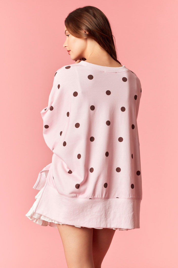 Woman wearing pink sweatshirt with burgundy polka dots and white mini skirt on plain background