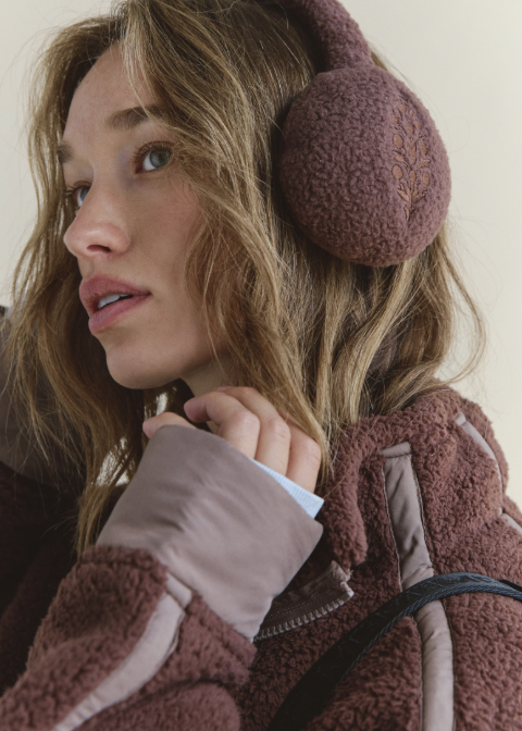 Woman wearing brown fleece plush ear warmers and brown fleece jacket on plain background