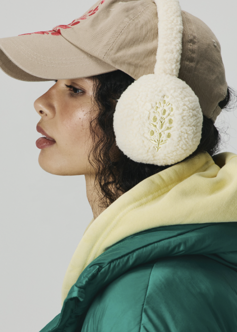 Woman wearing cream plush fleece ear warmers and green jacket on plain background
