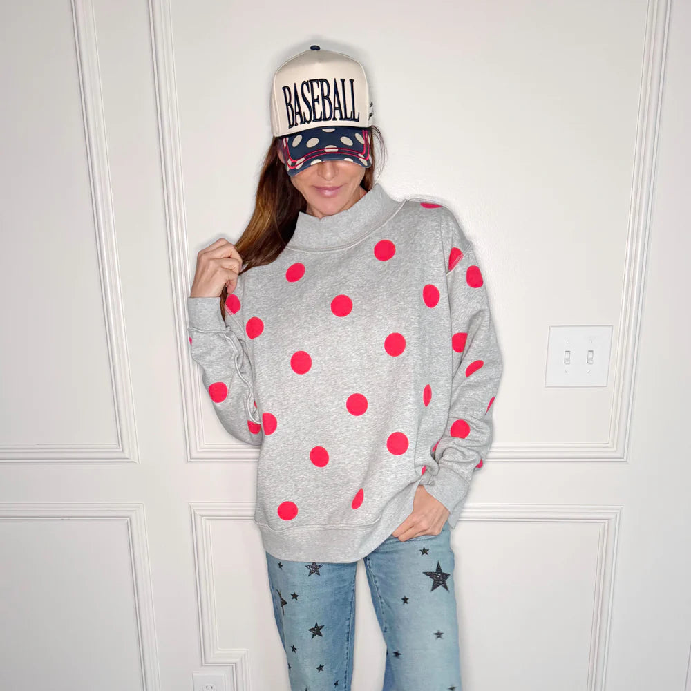 Woman wearing grey sweatshirt with red polka dots on plain background