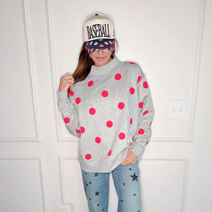 Woman wearing grey sweatshirt with red polka dots on plain background