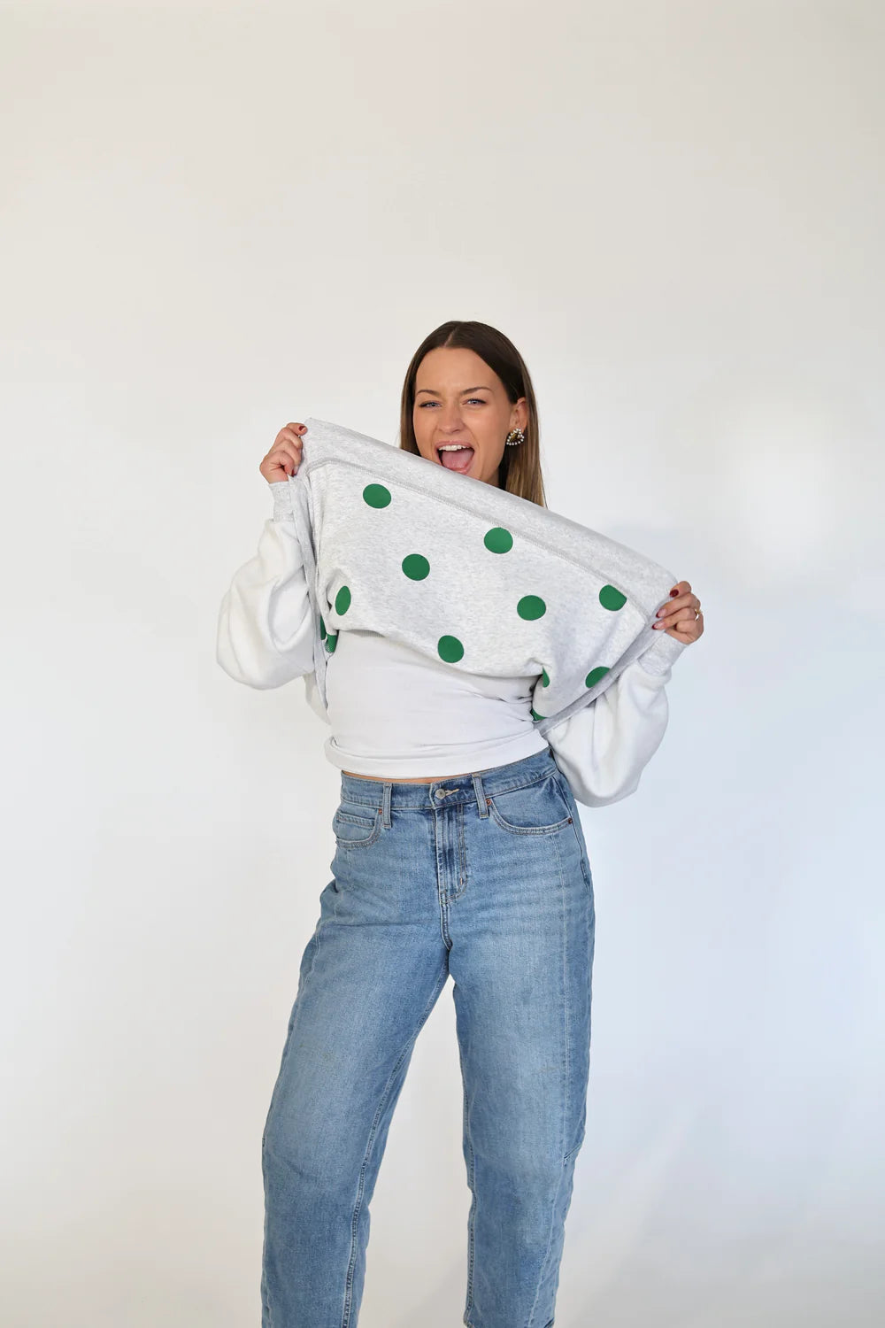 Person wearing a white sweater with green polka dots and blue jeans on a plain background