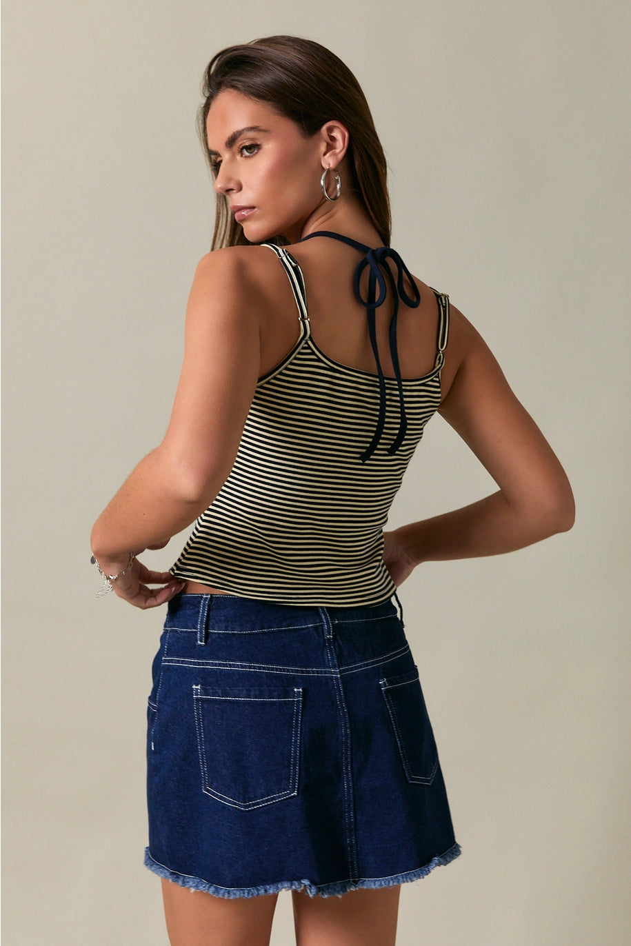 Woman wearing a striped tank top and denim skirt against a neutral background