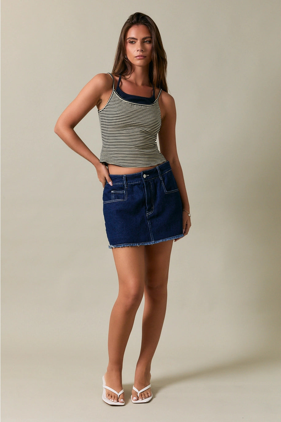 Woman wearing a striped tank top and denim skirt against a neutral background
