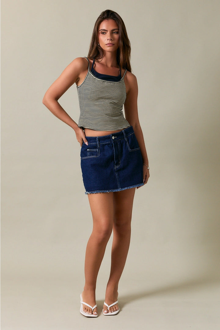Woman wearing a striped tank top and denim skirt against a neutral background