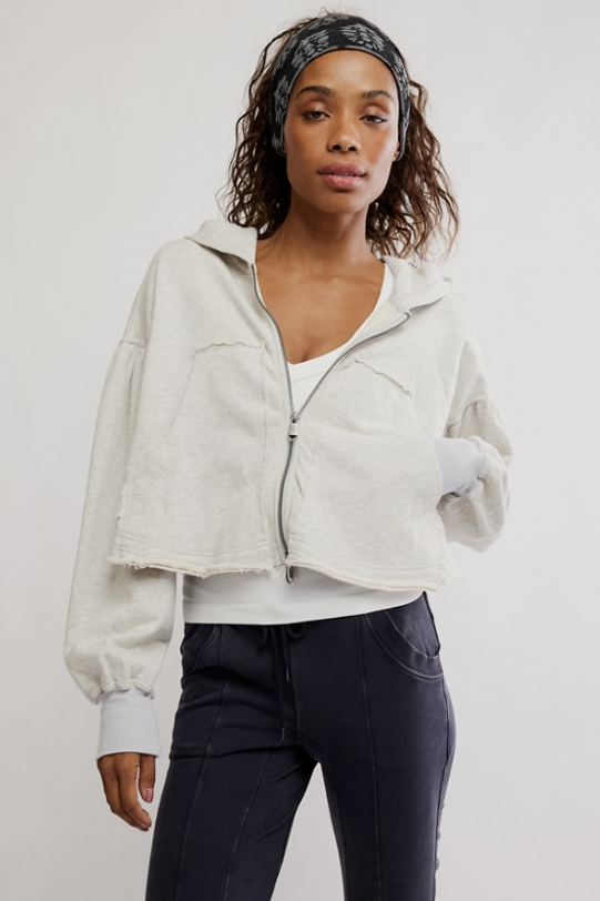 Woman wearing a light gray jacket, white shirt, and dark pants on a plain background