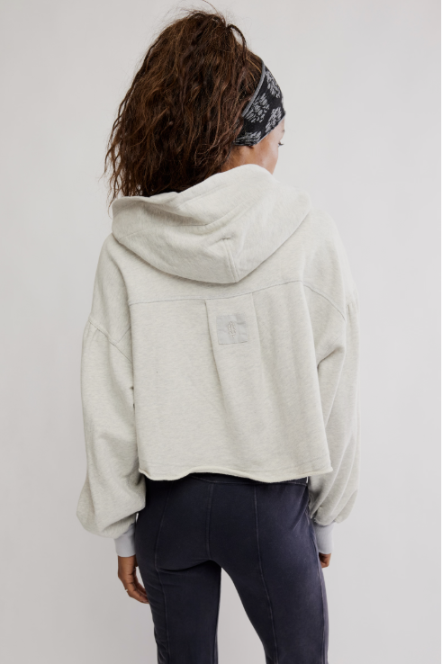 Person wearing a light gray hoodie with a brand logo on the back, standing against a plain background.