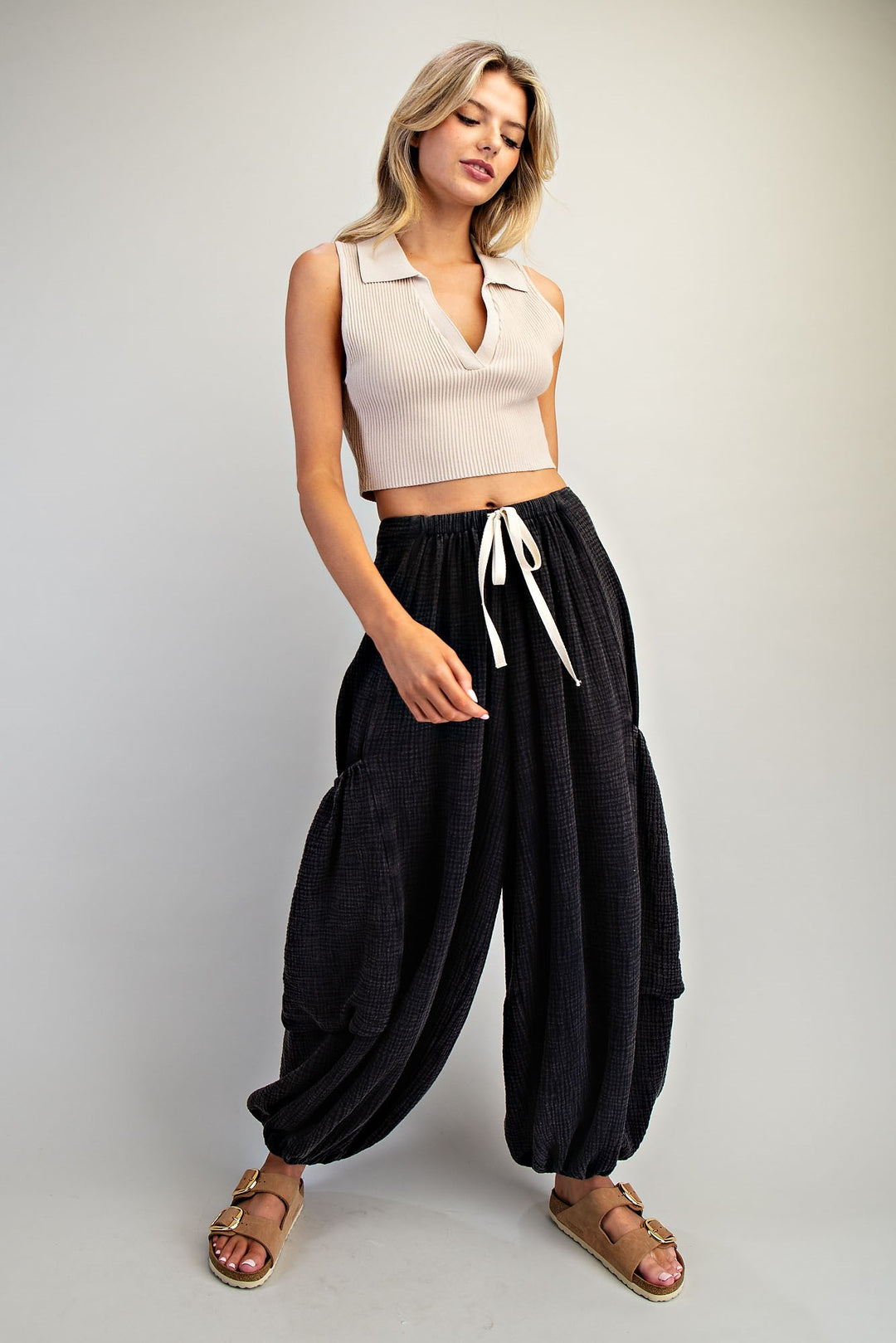 Woman wearing a beige sleeveless top and black harem pants on a plain background