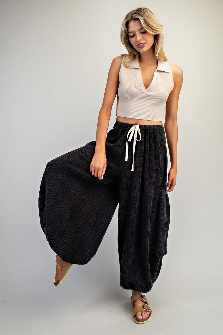 Woman wearing a beige sleeveless top and black wide-leg pants on a plain background