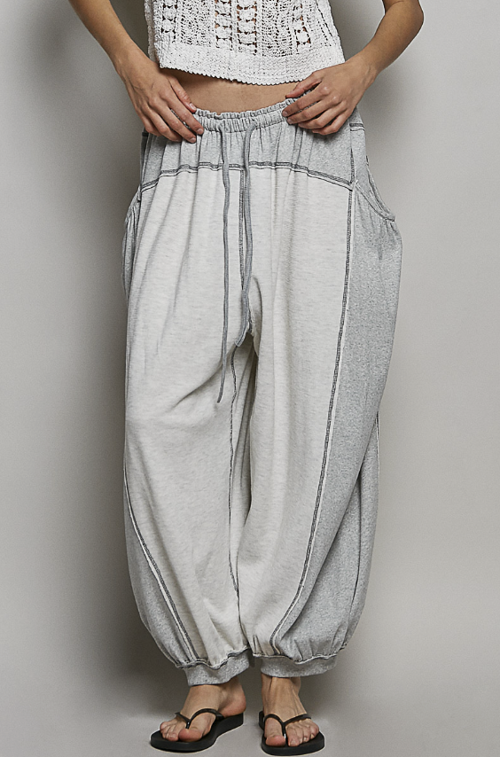 Person wearing light gray harem pants and a white lace top on a plain background
