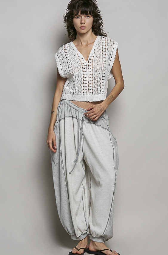 Woman wearing a white lace top and light gray pants against a plain background