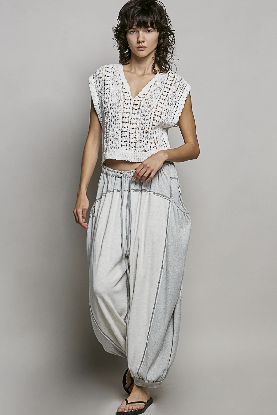 Woman wearing a white sleeveless top and light gray wide-leg pants against a plain background