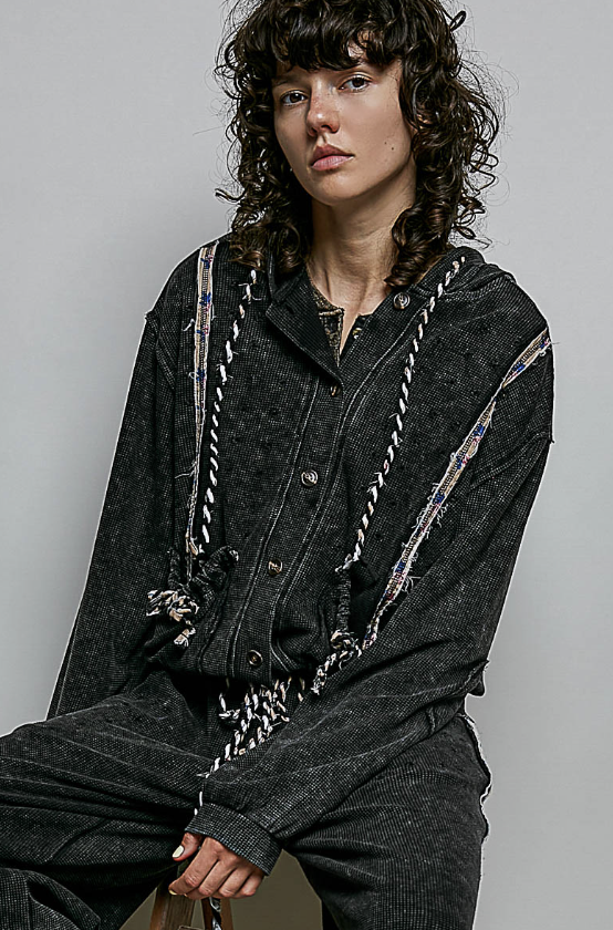 Woman wearing black waffle knit jacket with rope detailing on grey background