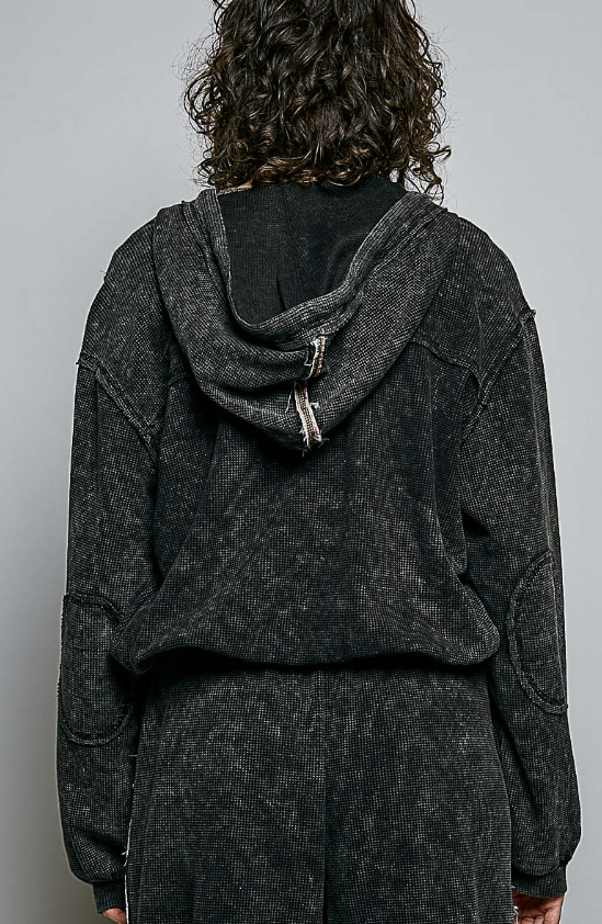 A person shown from the back wearing a dark charcoal gray hooded sweatshirt and matching sweatpants against a plain light gray studio background.