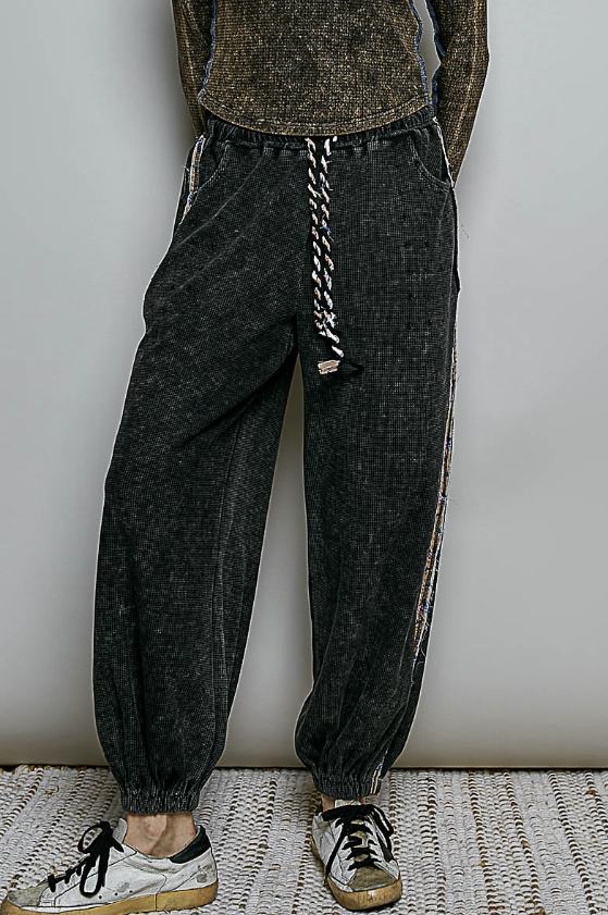 Woman wearing black waffle knit pants and brown top on plain background