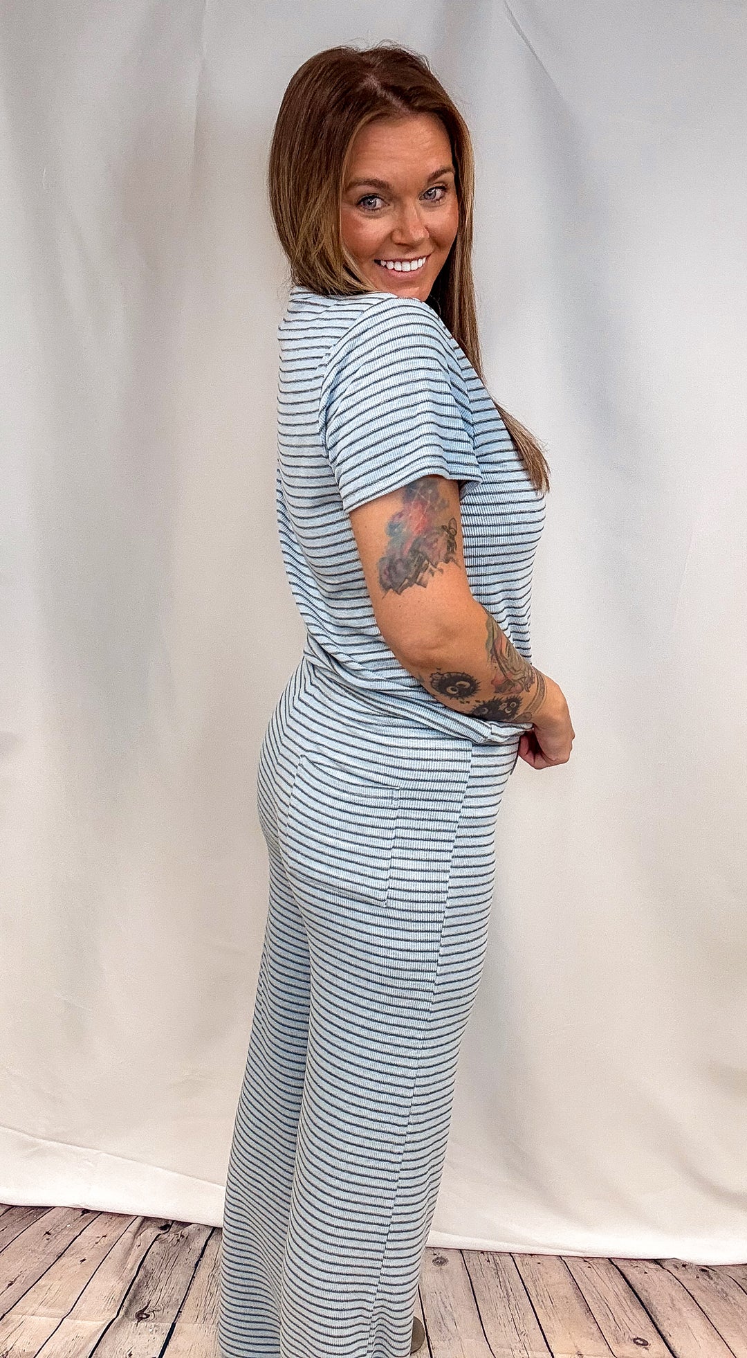 A woman modeling a light blue and white striped short-sleeve maxi dress, posing in front of a white fabric backdrop.