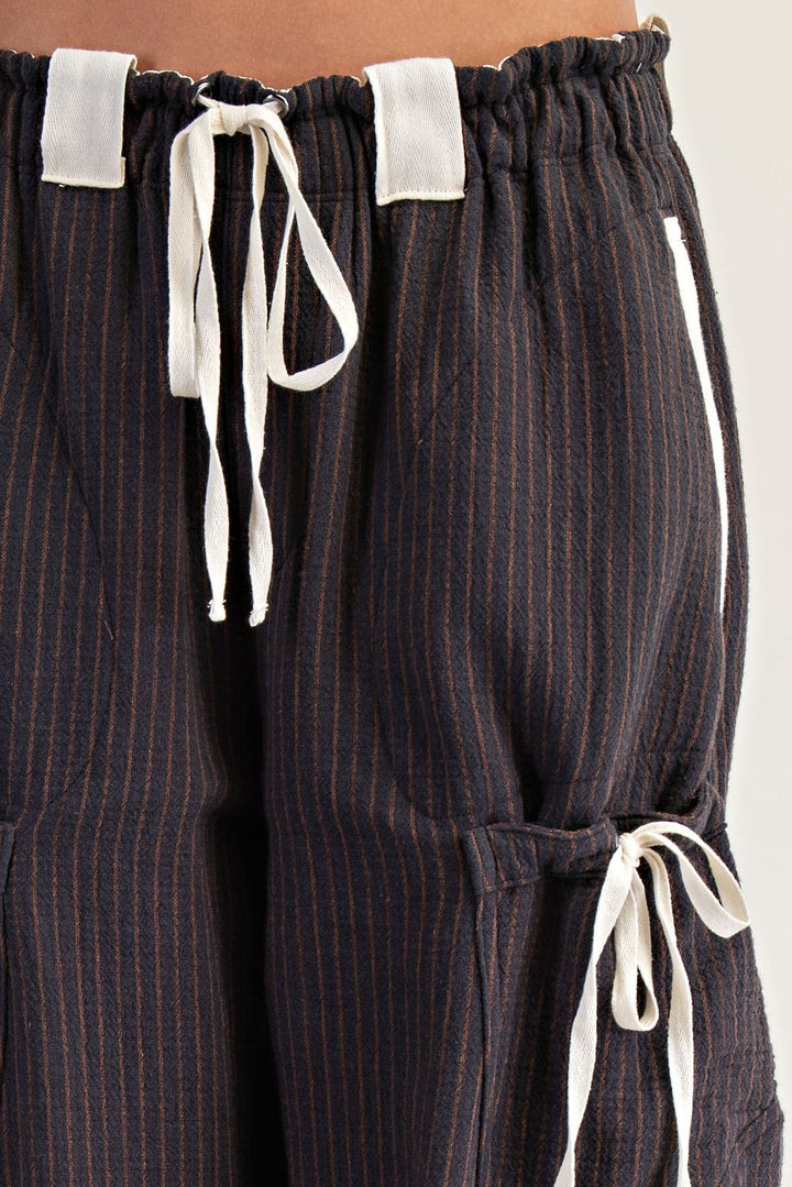 Close-up of dark navy pinstriped pants with white drawstrings and white side tabs, shown on a model.