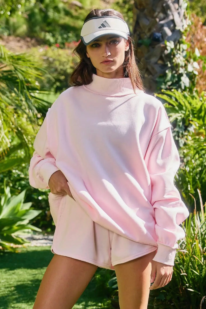 Person wearing a pink sweatshirt and shorts set with a visor outdoors.