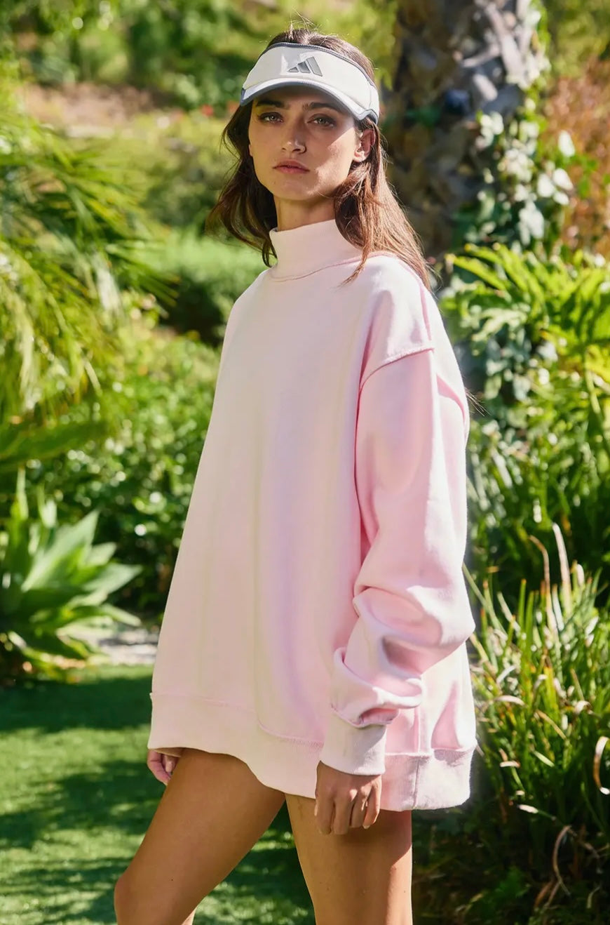 Woman wearing a light pink oversized sweater and white visor in a garden setting