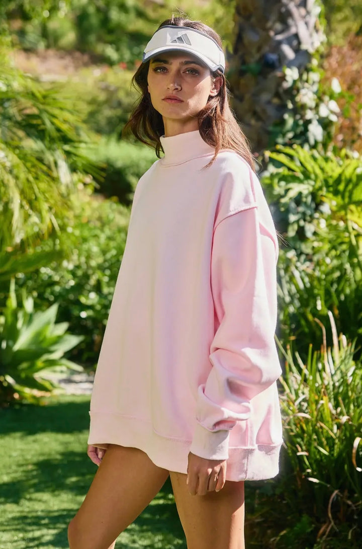 Woman wearing a light pink oversized sweater and white visor in a garden setting
