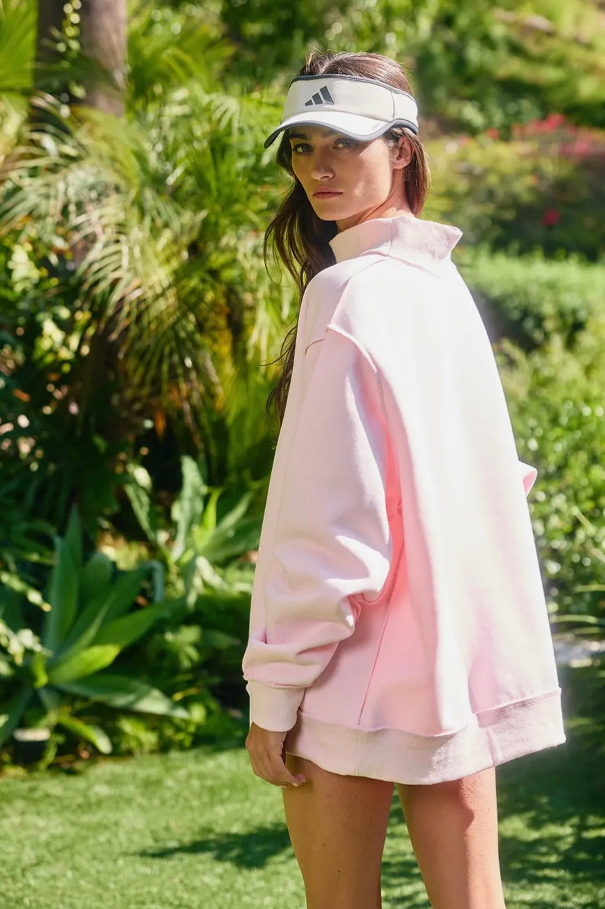 Woman wearing a light pink jacket and visor in a garden setting