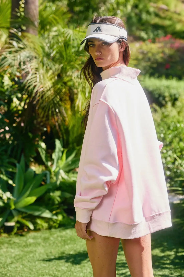 Woman wearing a light pink jacket and visor in a garden setting