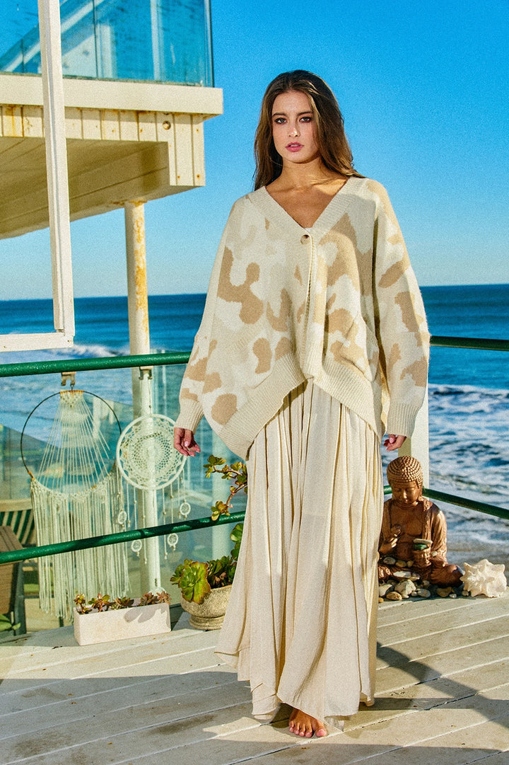 Woman wearing oversize camo cardigan and linen skirt standing outside