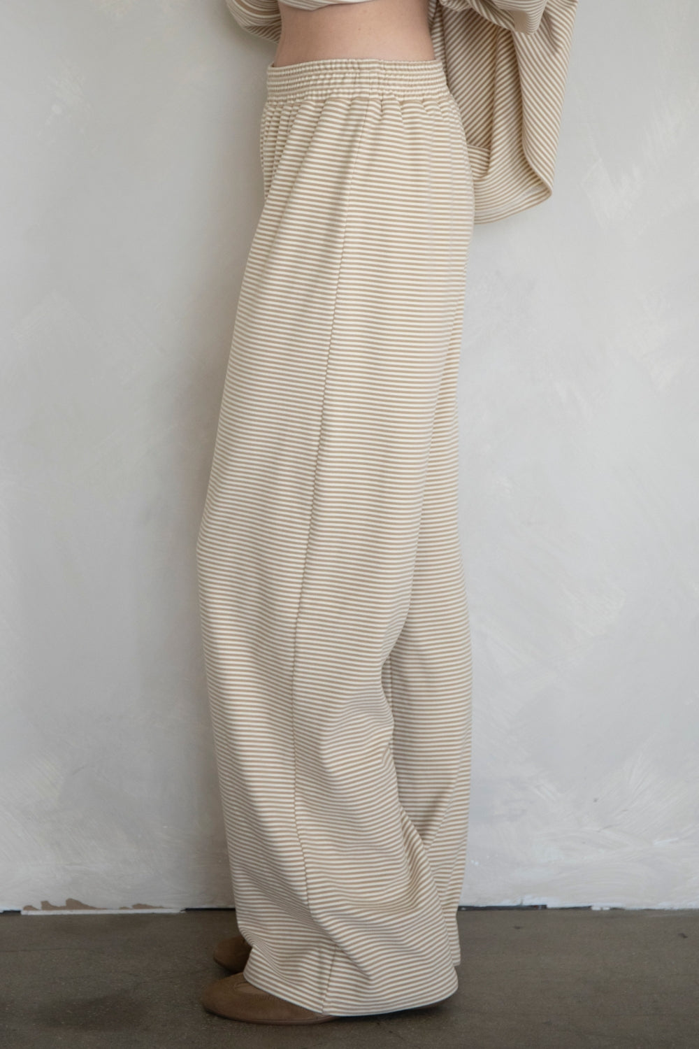 Person wearing beige striped pants against a white wall