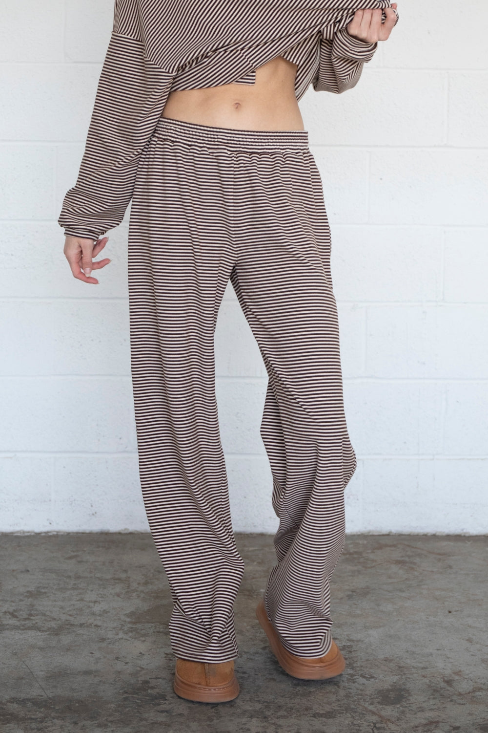Person wearing a striped outfit with wide-leg pants against a white wall.