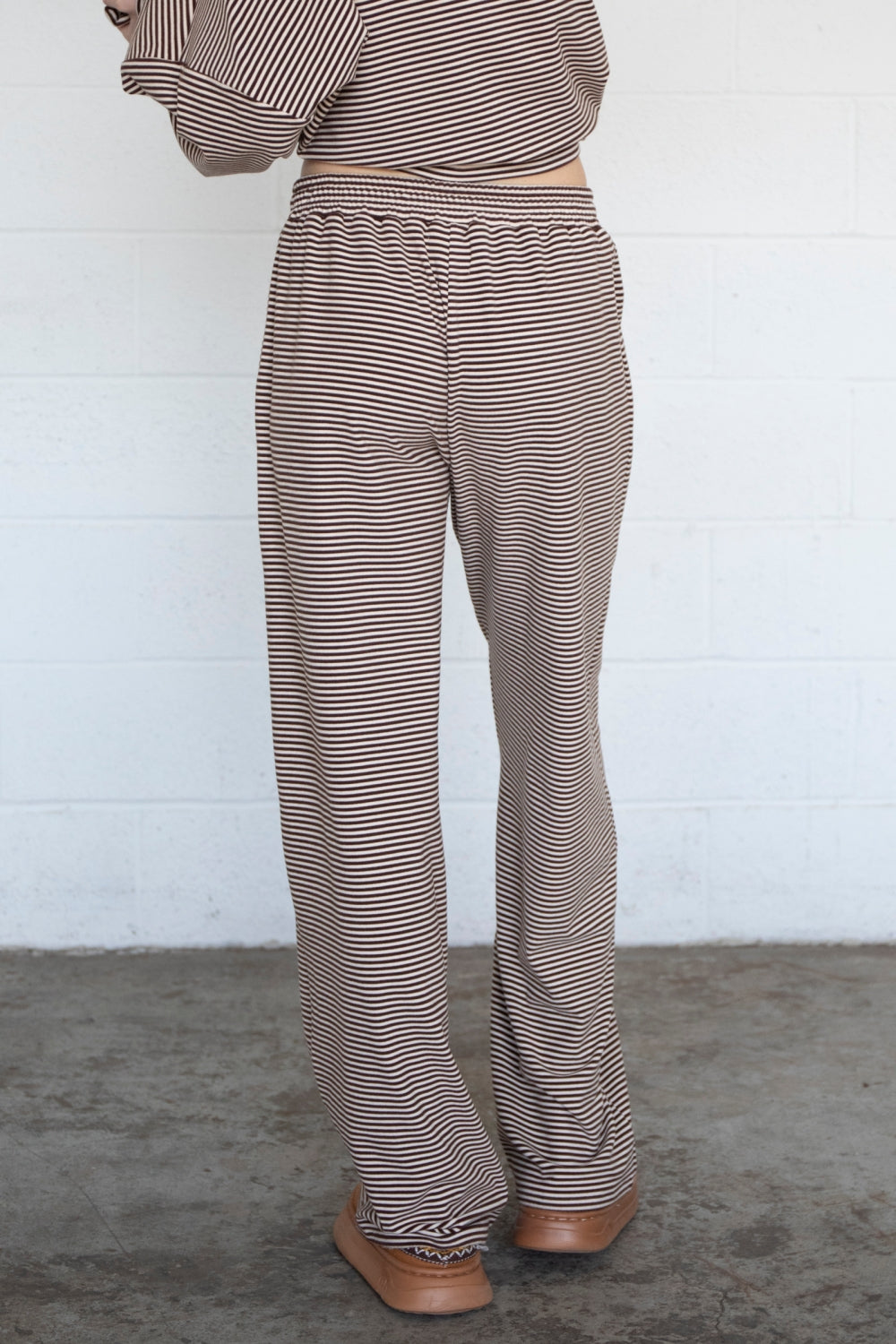 Person wearing brown and white striped pants against a white wall.